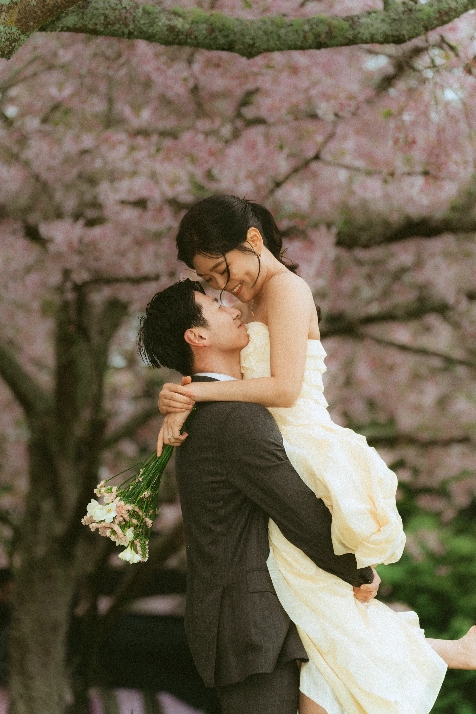 Emily being lifted by Benny beneath pink blossom trees