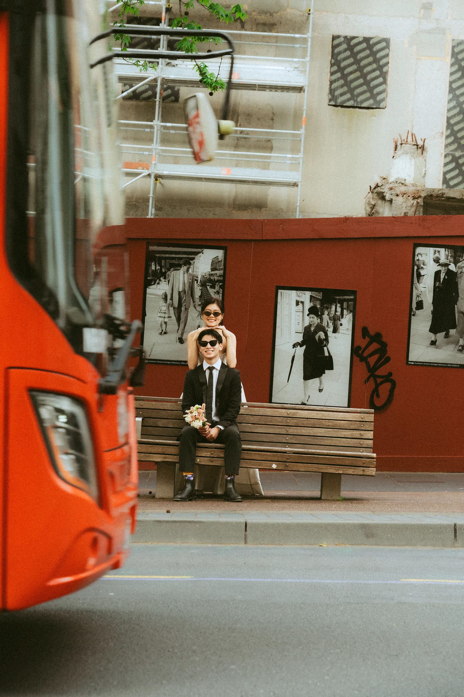 Emily and Benny posing by a city bench as a red bus passes