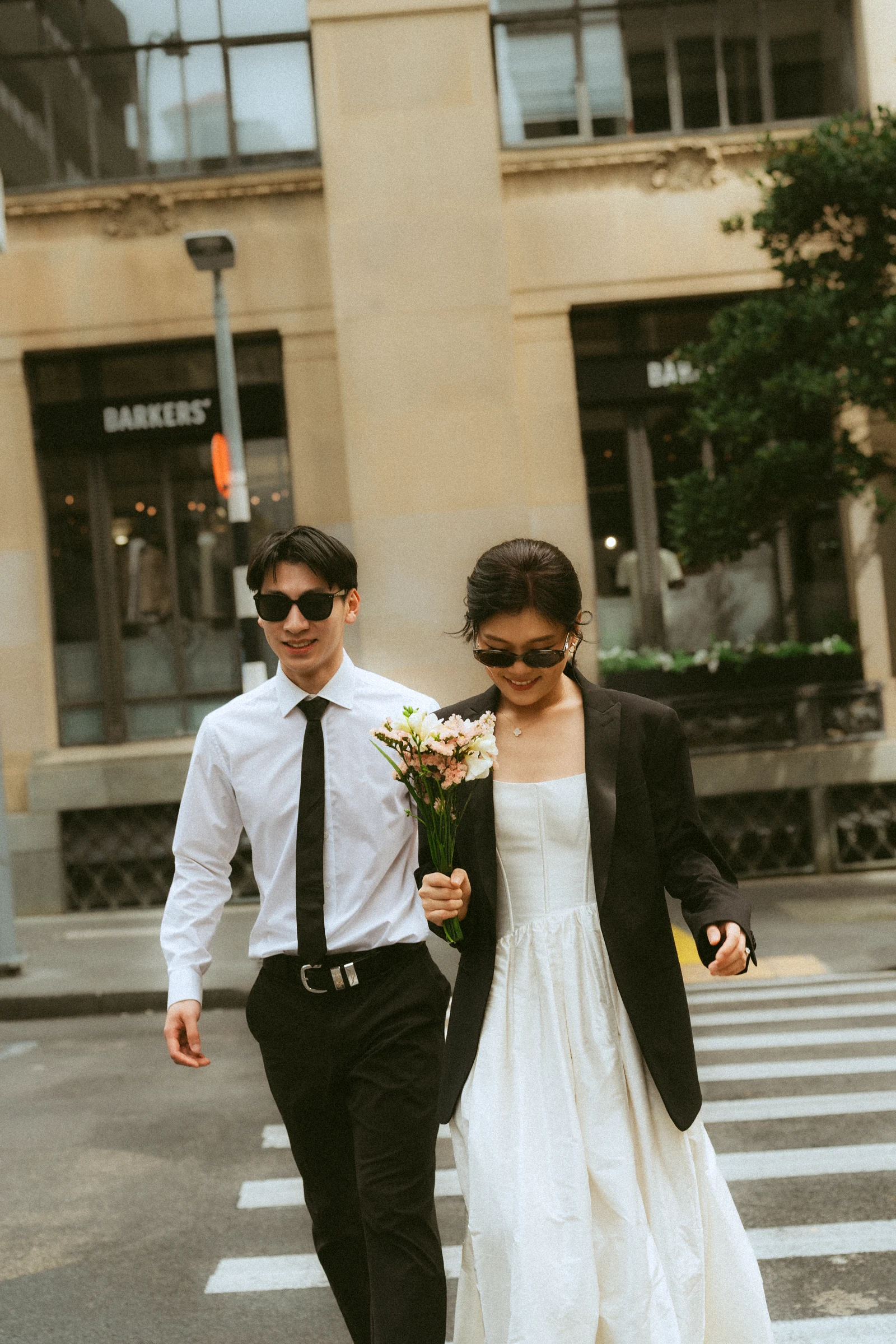 Emily and Benny wearing sunglasses and walking across a city crossing